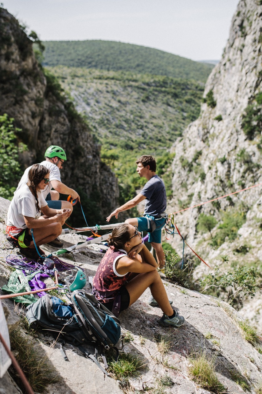 group of climbers resting and preparing gear on rocky ledge beside steep canyon walls