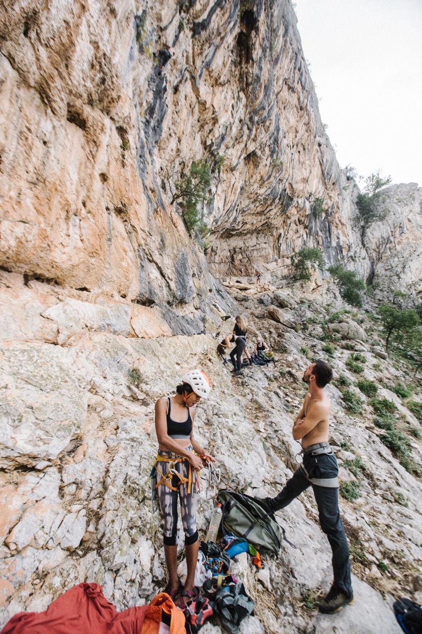woman wearing helmet and climbing gear preparing ropes as man watches on rocky cliffside with other climbers