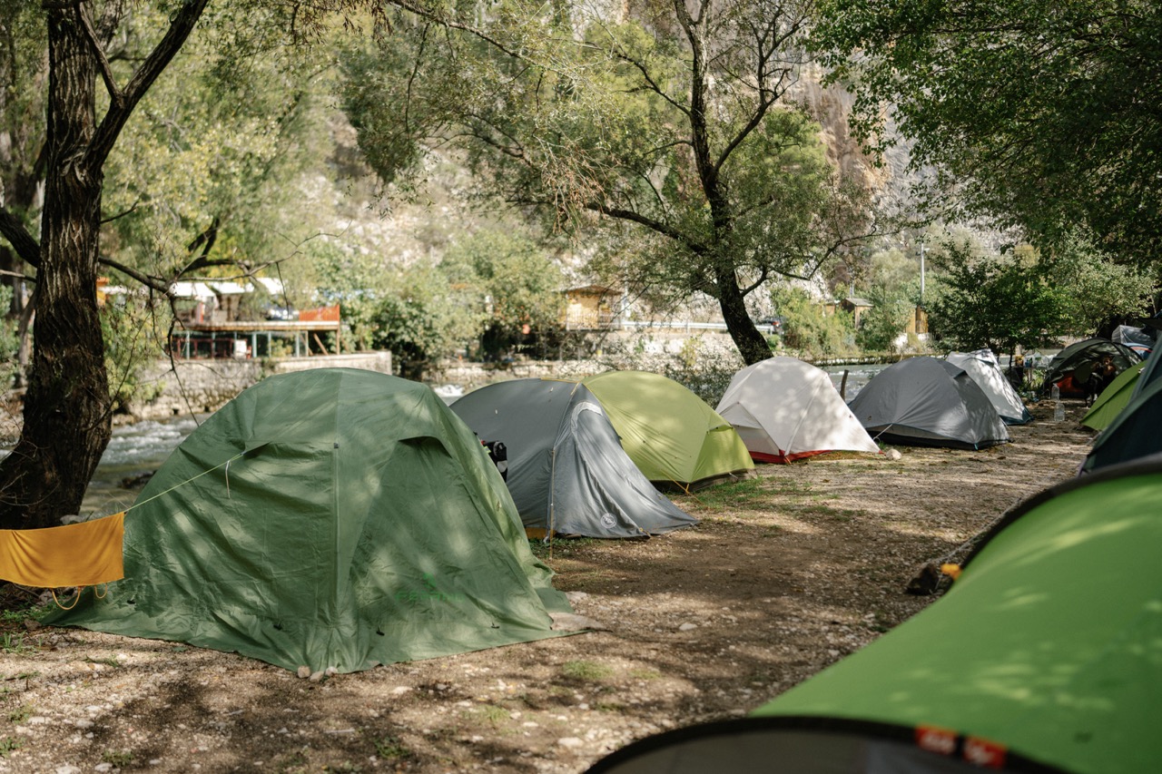 row of colorful camping tents pitched on dirt ground near trees and a river