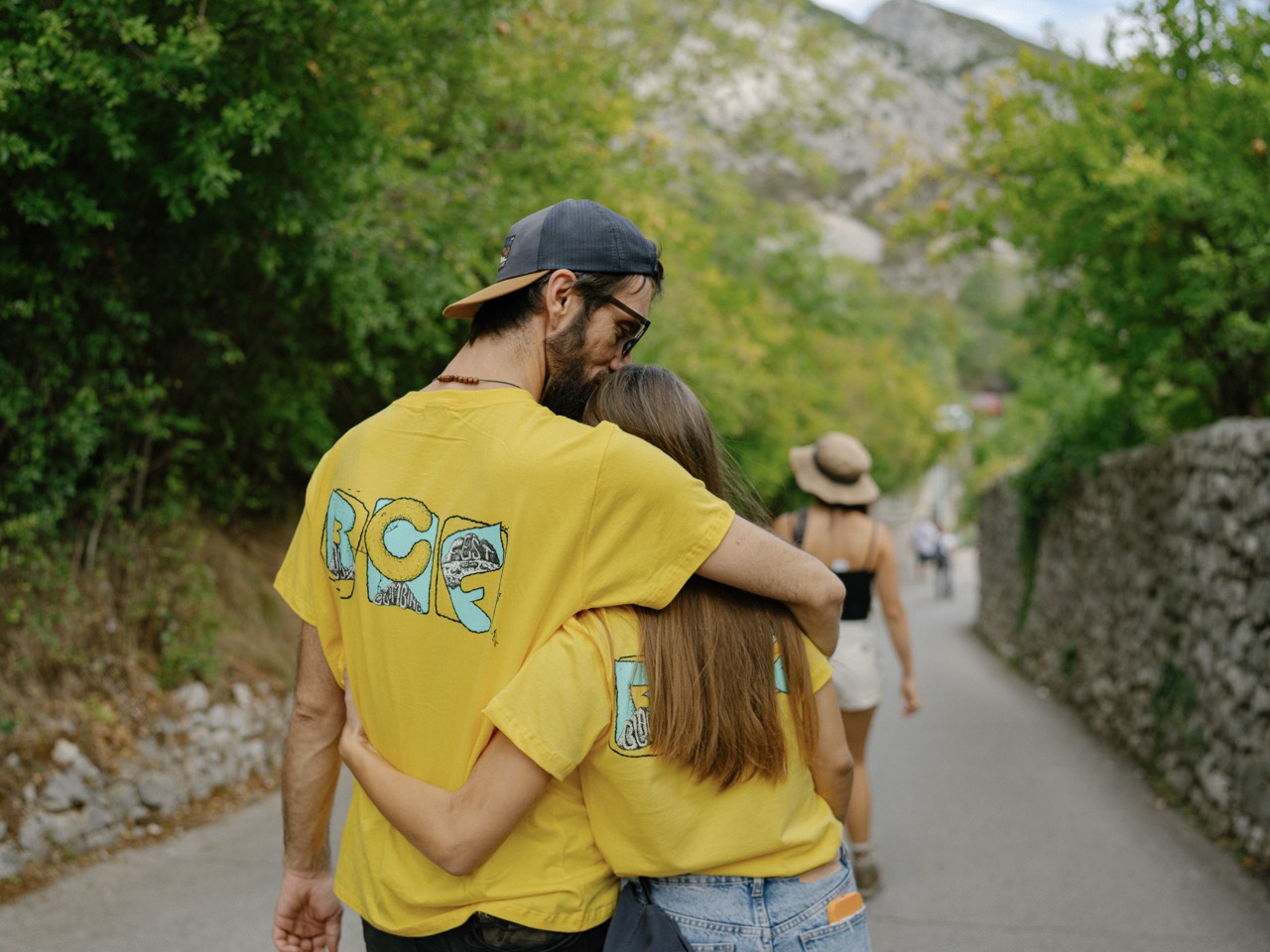 couple in matching yellow shirts embracing and walking on a pathway surrounded by greenery