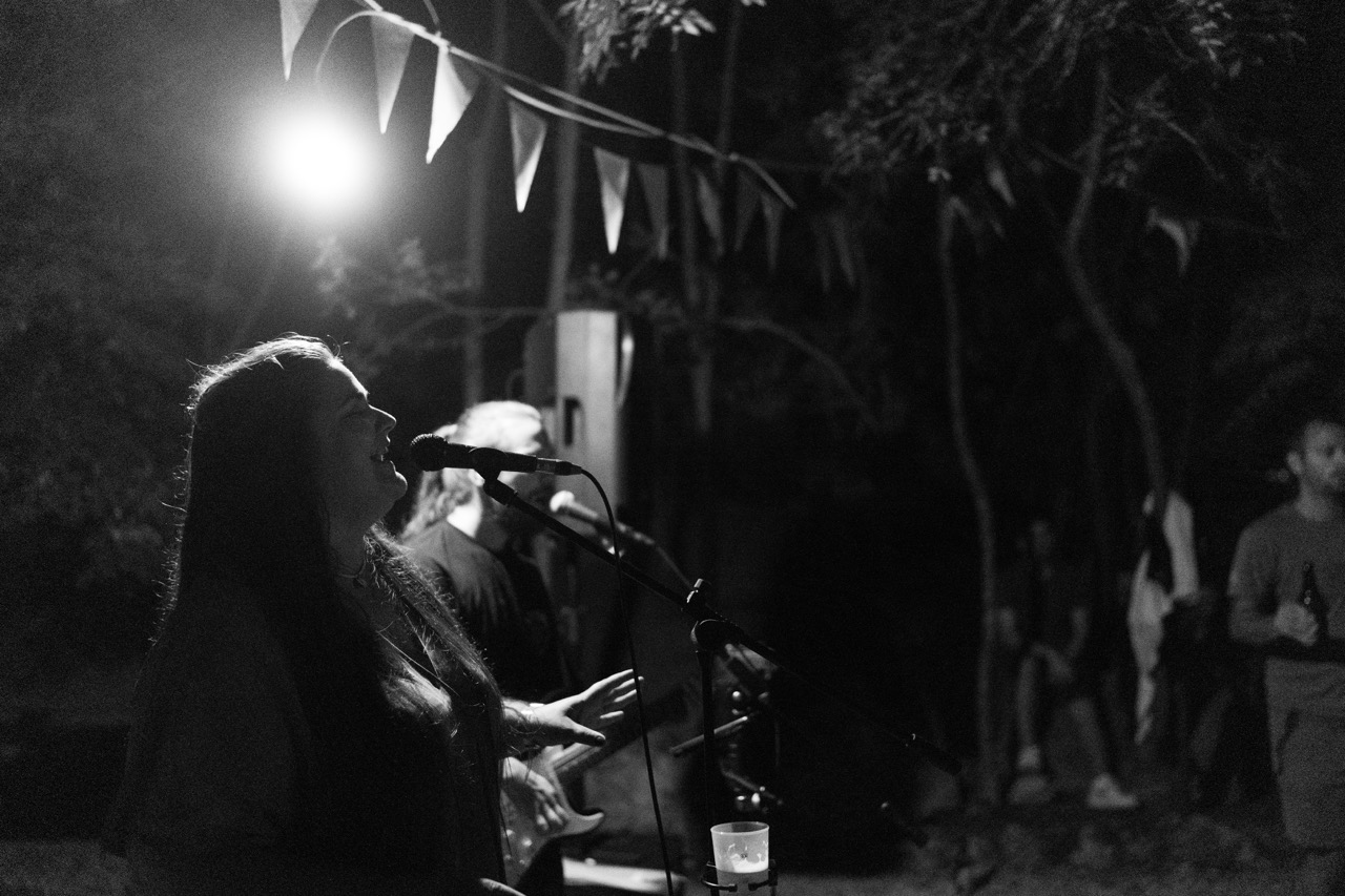 woman singing into microphone at outdoor night concert with string lights and bunting flags