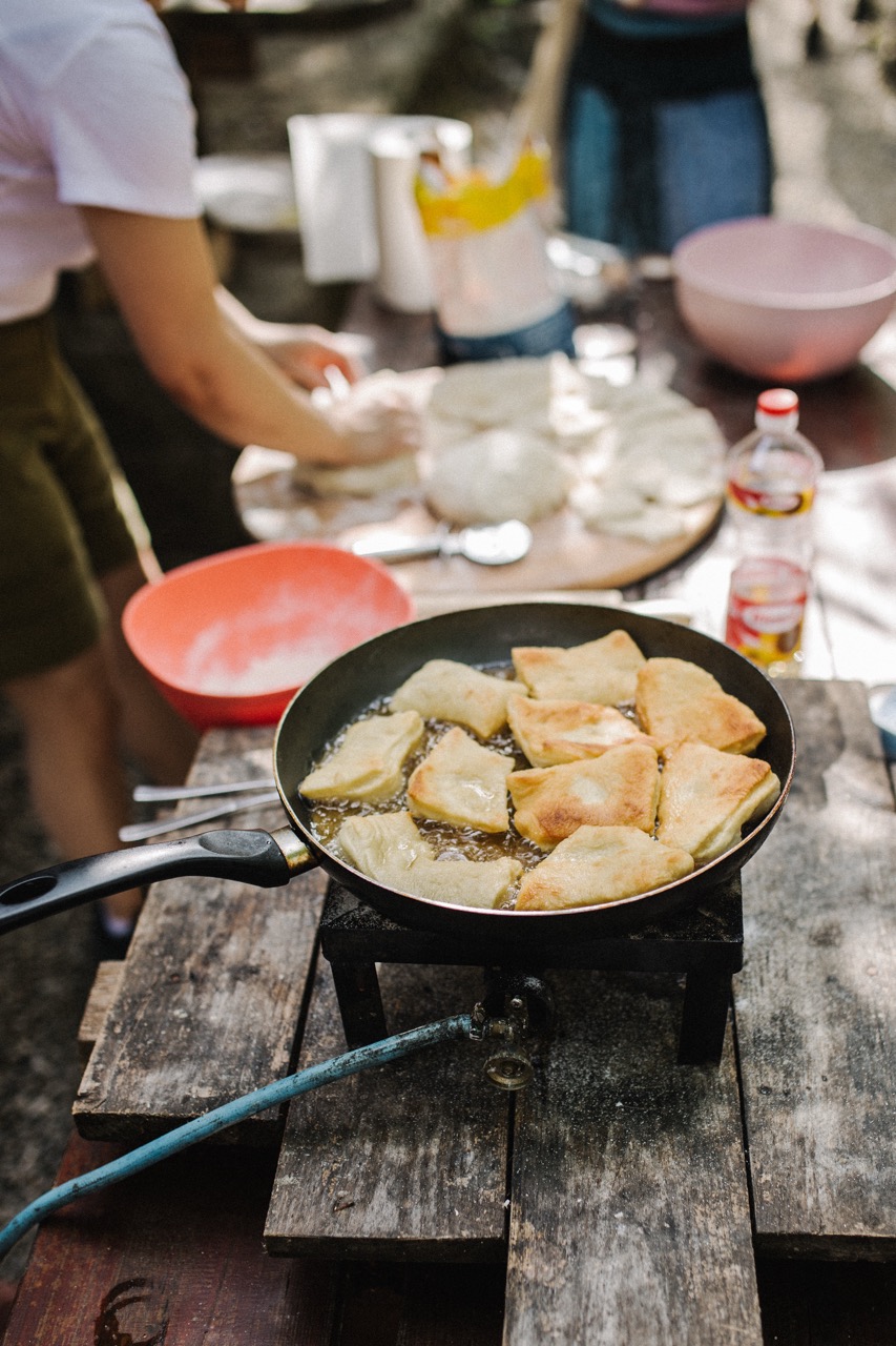fried dough pieces cooking in a pan on a gas burner outdoors