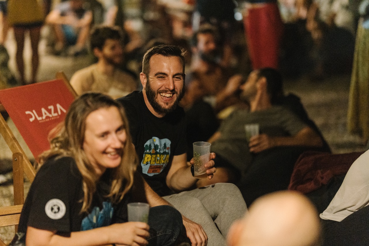 group of people enjoying drinks and laughing at an outdoor event during the evening