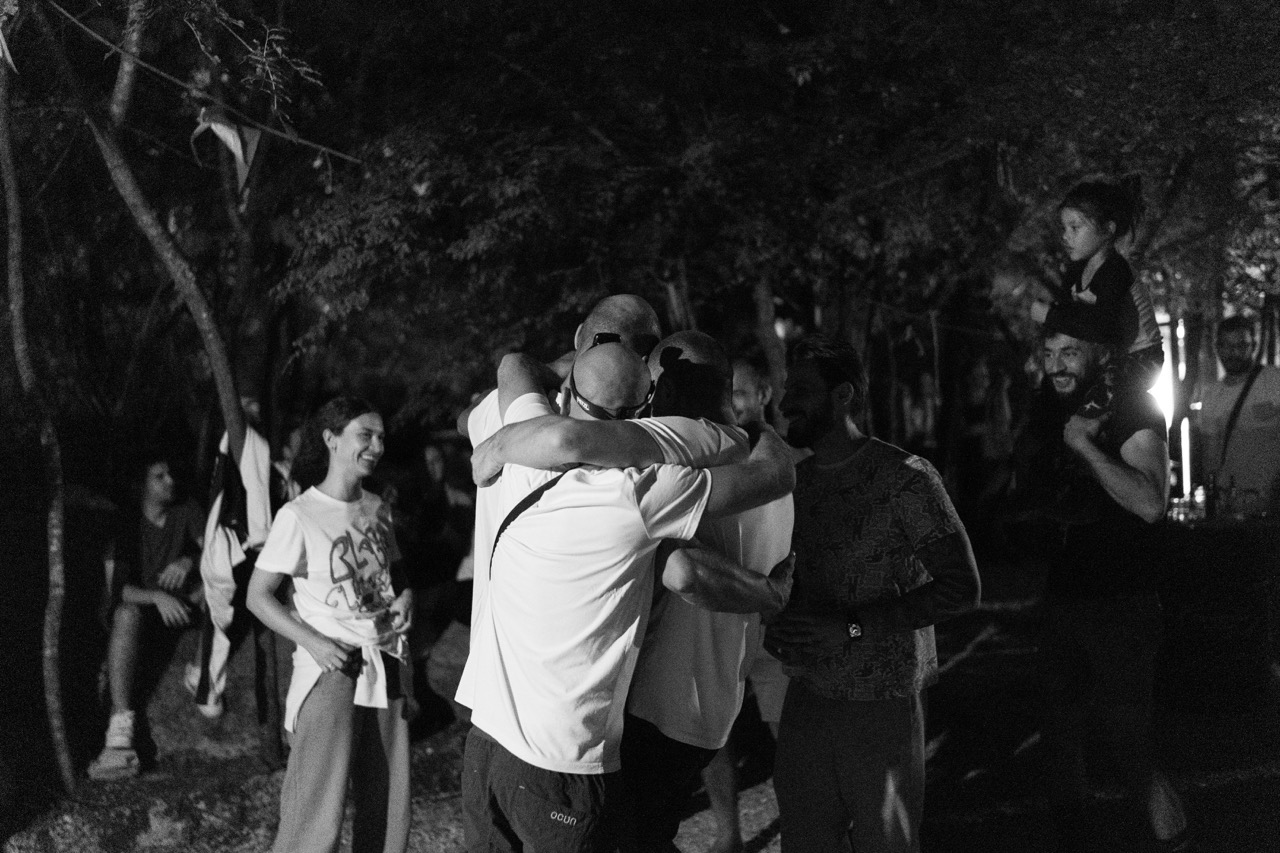 group of friends hugging and smiling outdoors at night with trees in the background