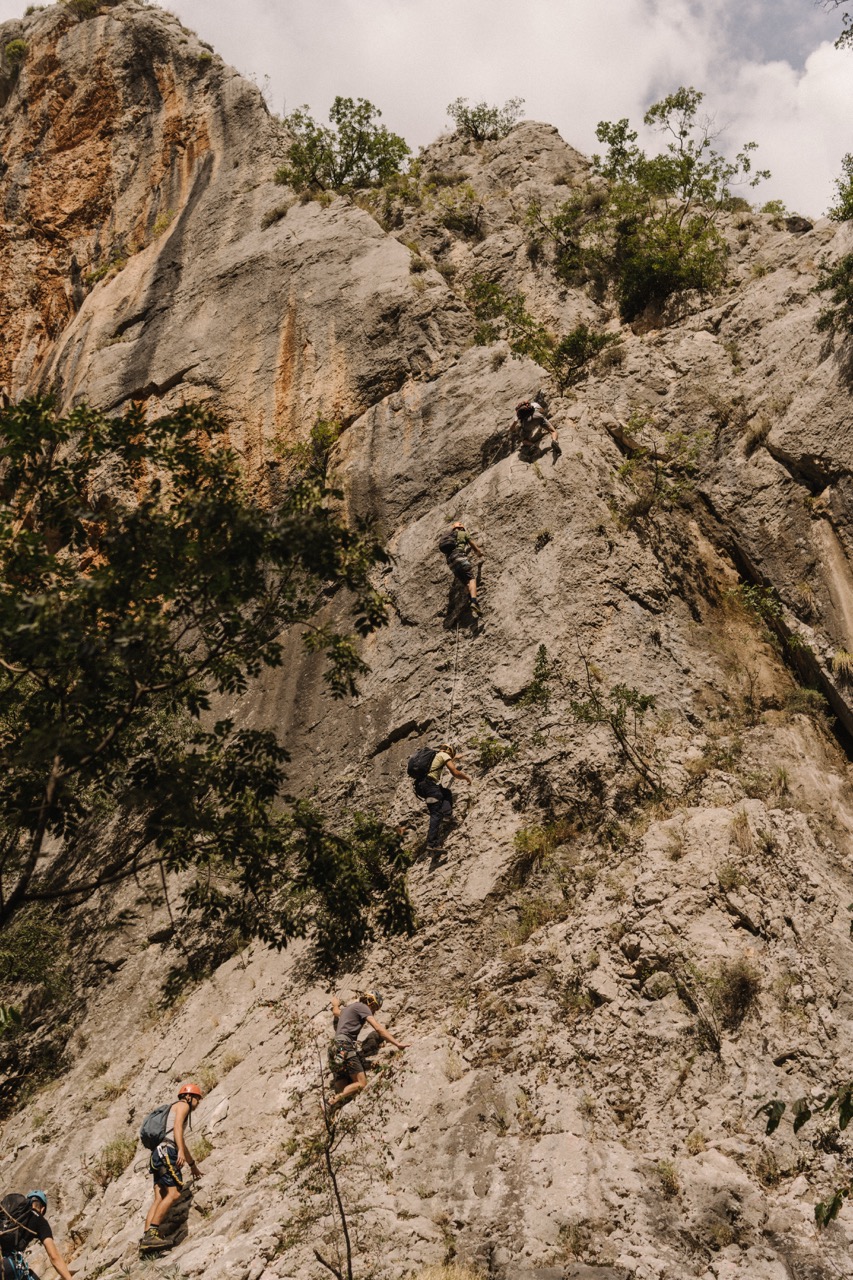 group of climbers ascending a large rocky cliff surrounded by sparse vegetation and trees