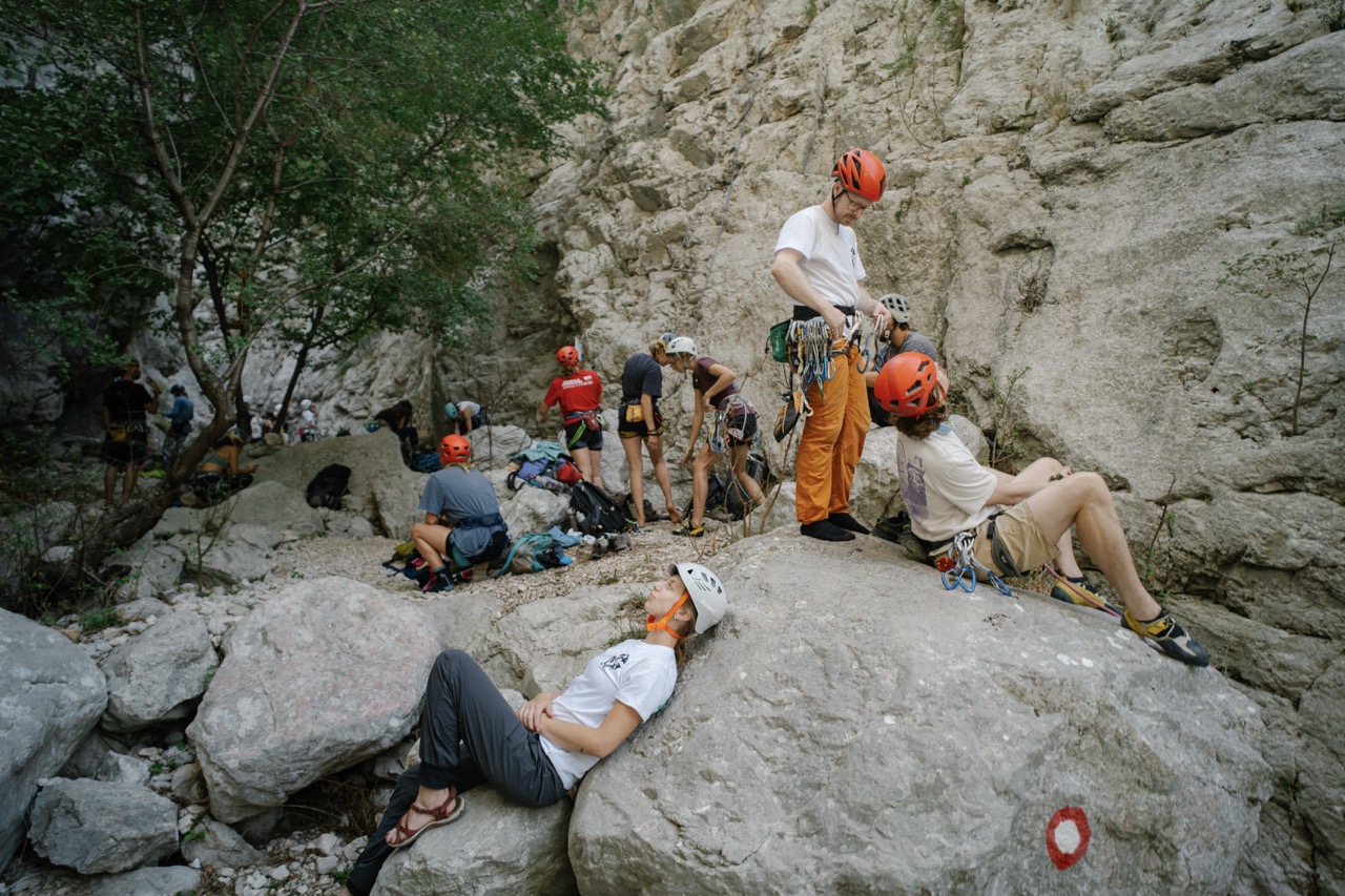 group of climbers resting and preparing near a rocky cliff wearing helmets and climbing gear