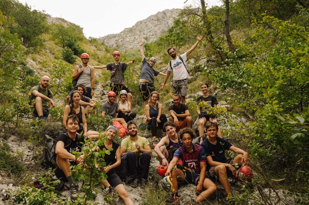 group of young hikers resting on rocky terrain surrounded by green foliage and mountains