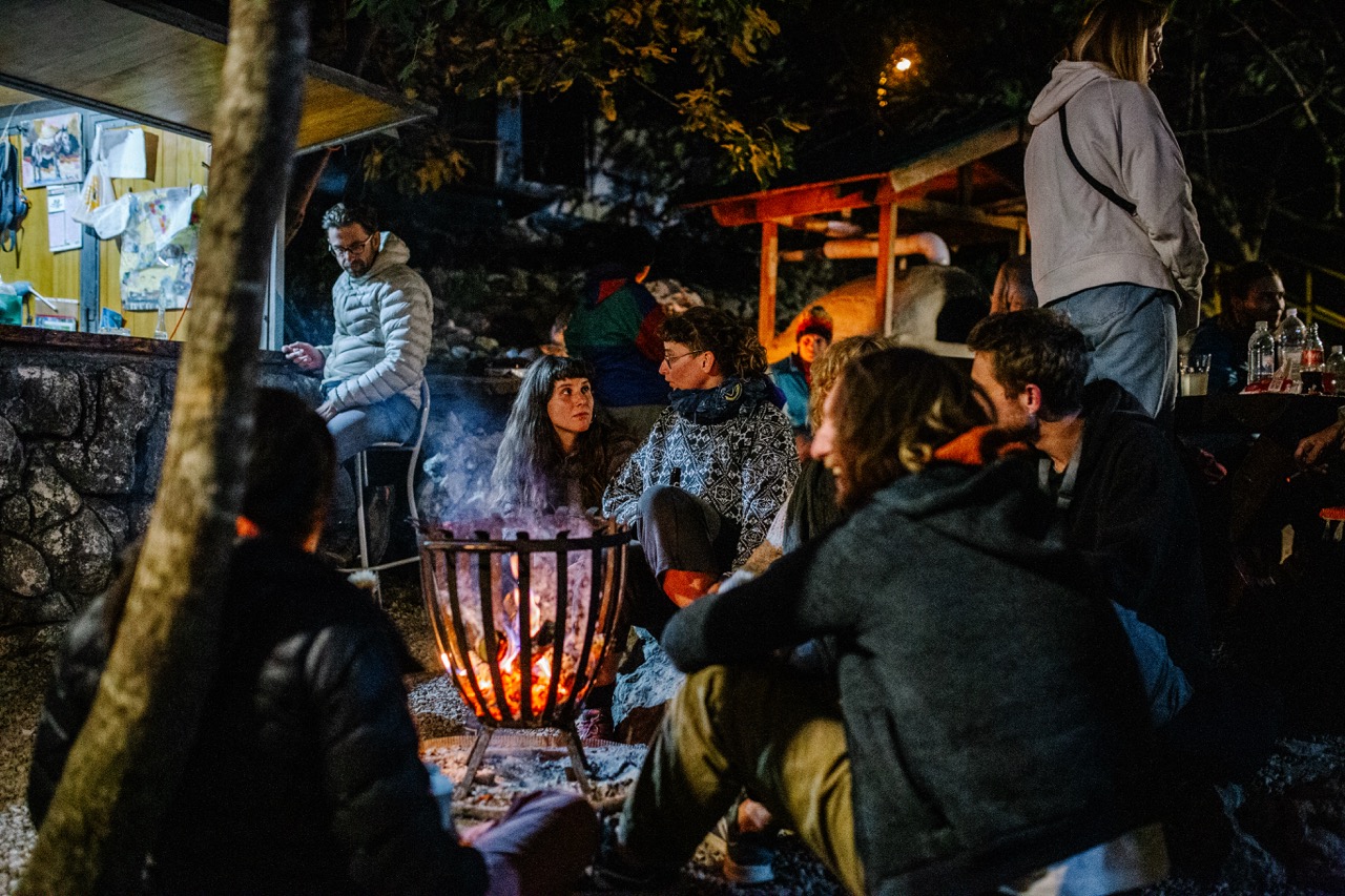 group of people gathered around an outdoor fire pit at night with warm lighting