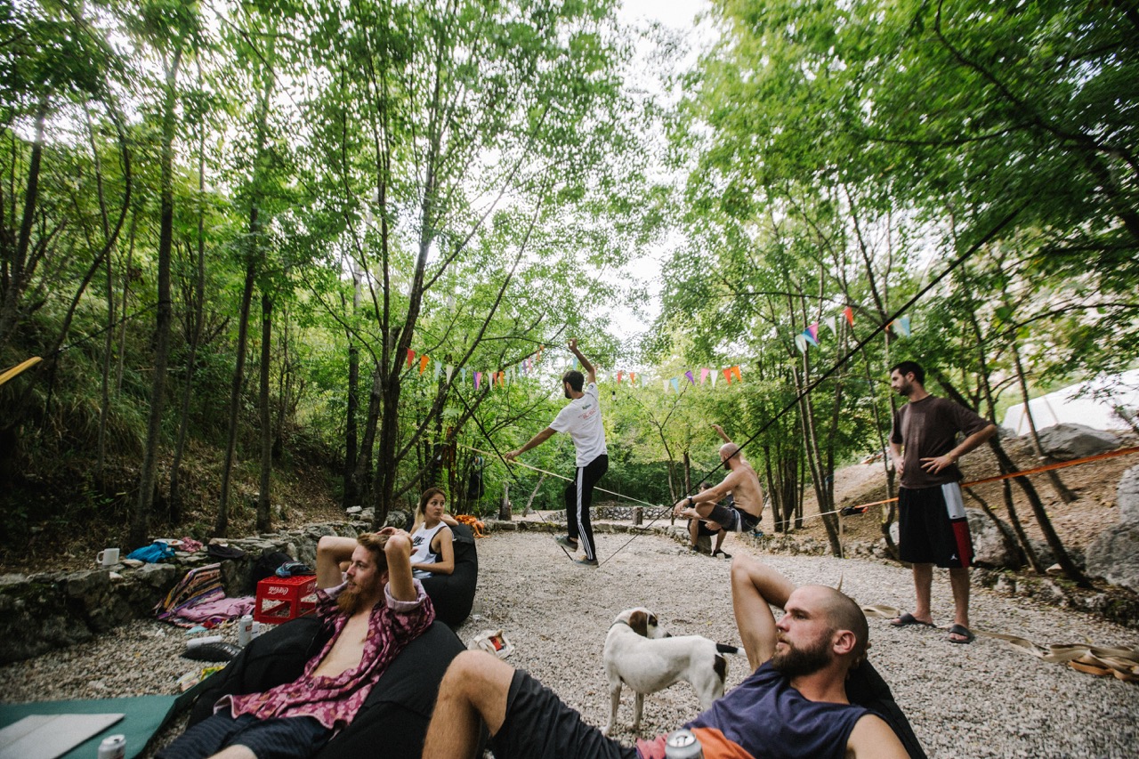 people relaxing and walking on slacklines in a wooded outdoor area with colorful bunting overhead
