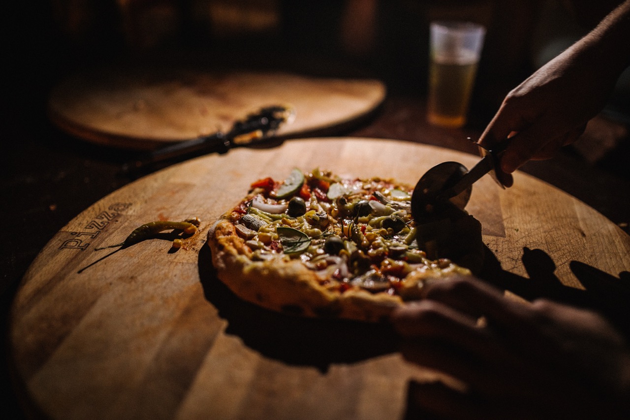 person cutting a freshly baked vegetable pizza on a wooden pizza board