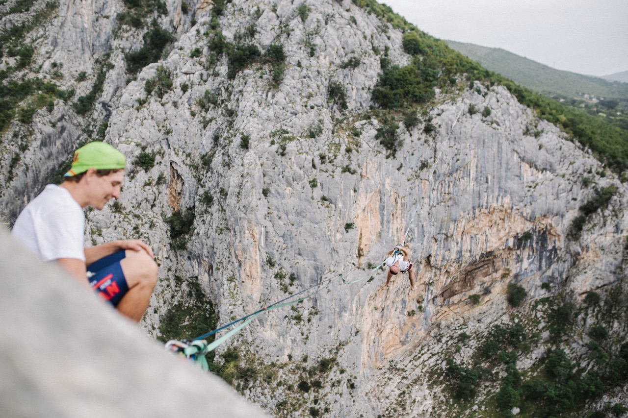 person hanging and swinging high above rocky cliffside on a slackline with safety harness