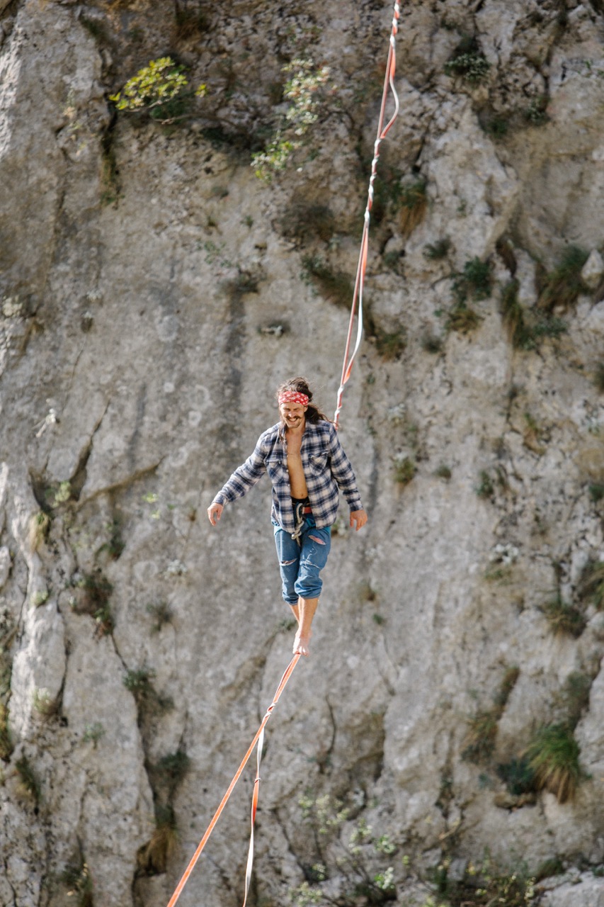 man balancing barefoot on a highline rope against a rocky cliff background