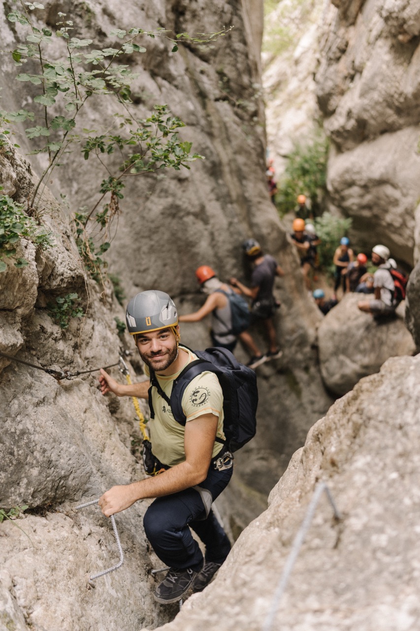 man climbing rocky canyon wall with helmet and backpack in a group adventure