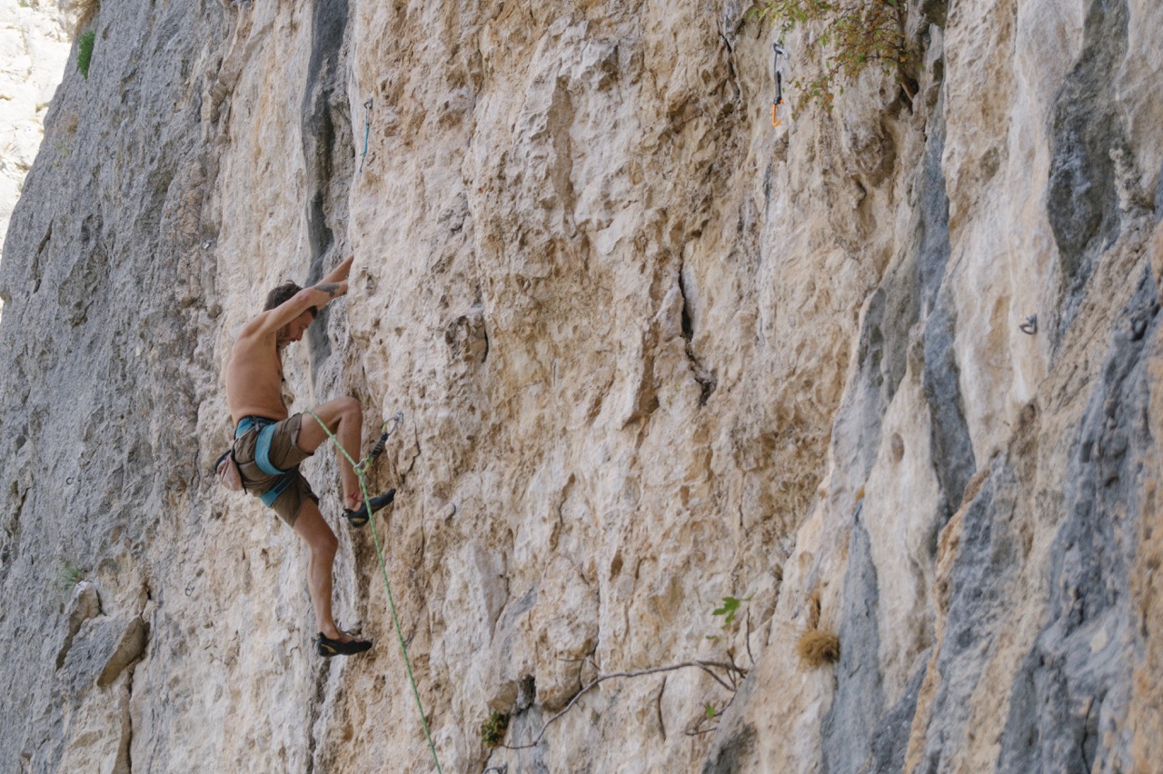 man climbing steep rocky cliff wearing safety harness and climbing shoes