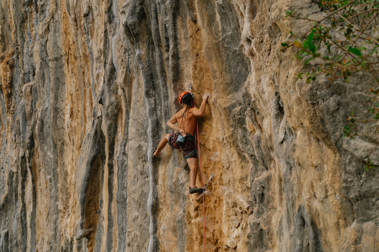 man climbing steep rocky cliff wearing helmet and harness