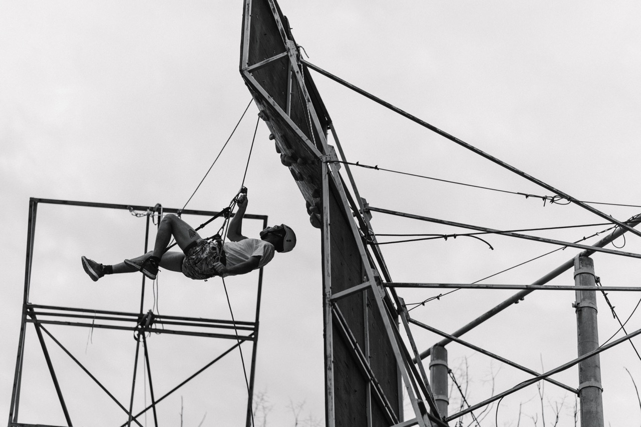 man climbing and hanging from a vertical climbing wall with safety harness in cloudy outdoor setting