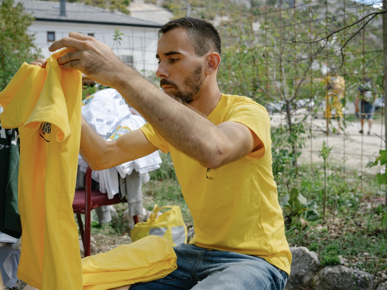 man wearing yellow t-shirt carefully folding a yellow t-shirt outdoors