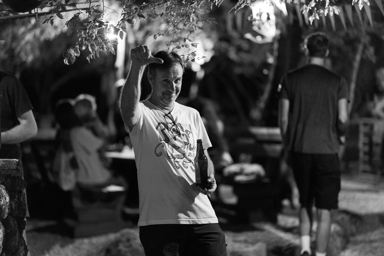man at outdoor nighttime gathering holding a bottle and making a thumbs down gesture