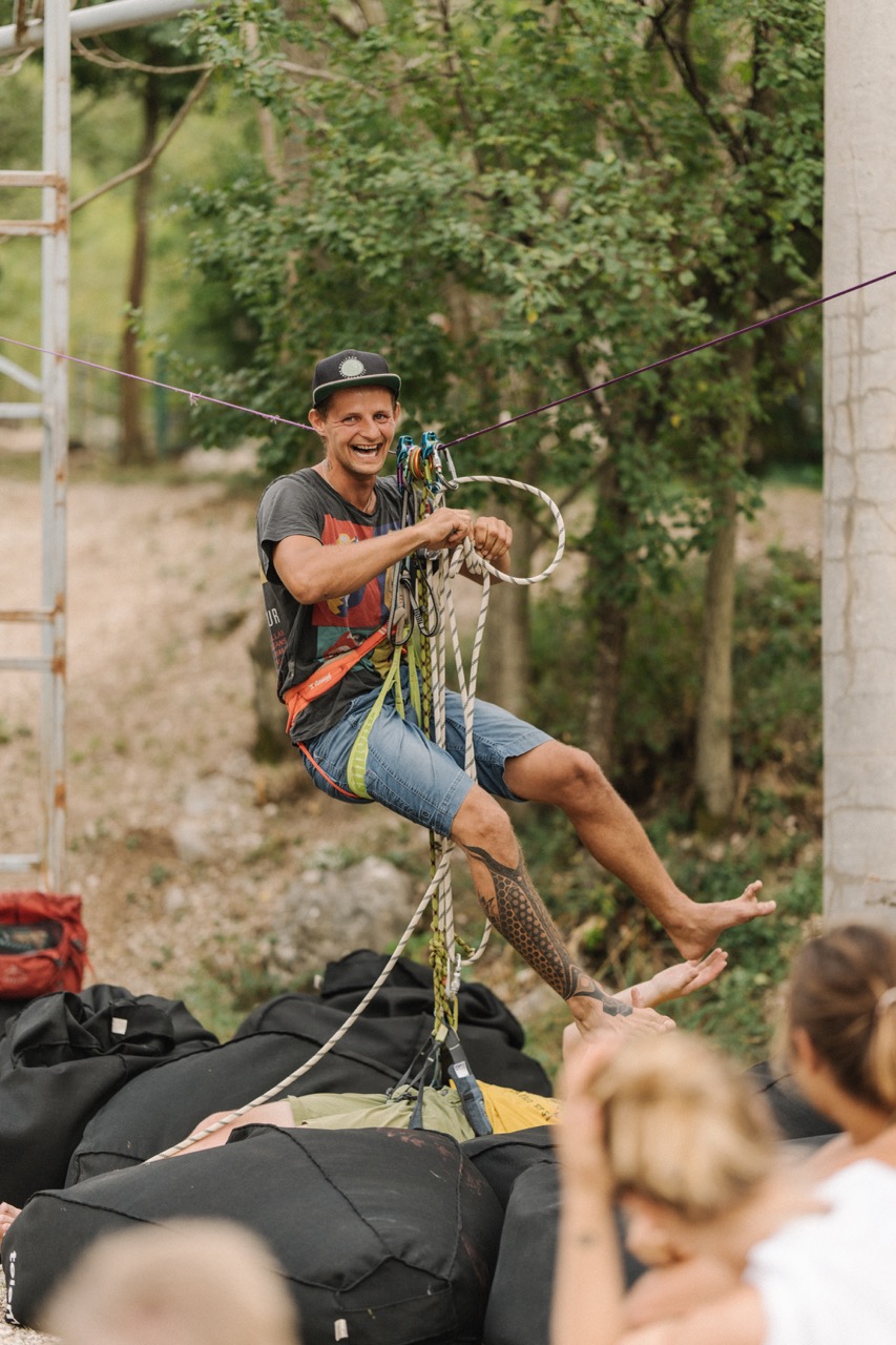 man wearing harness and helmet smiling while preparing for slackline activity outdoors