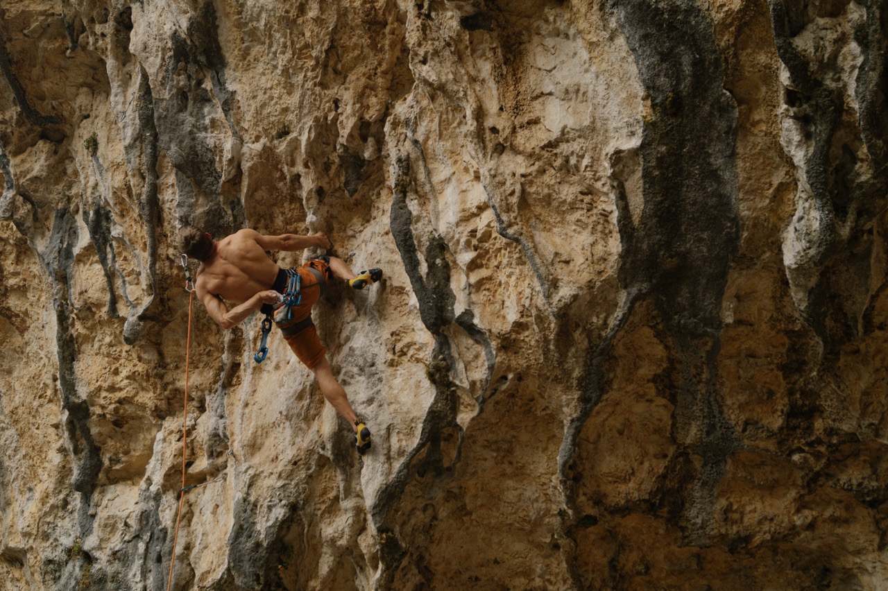 man climbing challenging rock wall with safety harness and climbing shoes