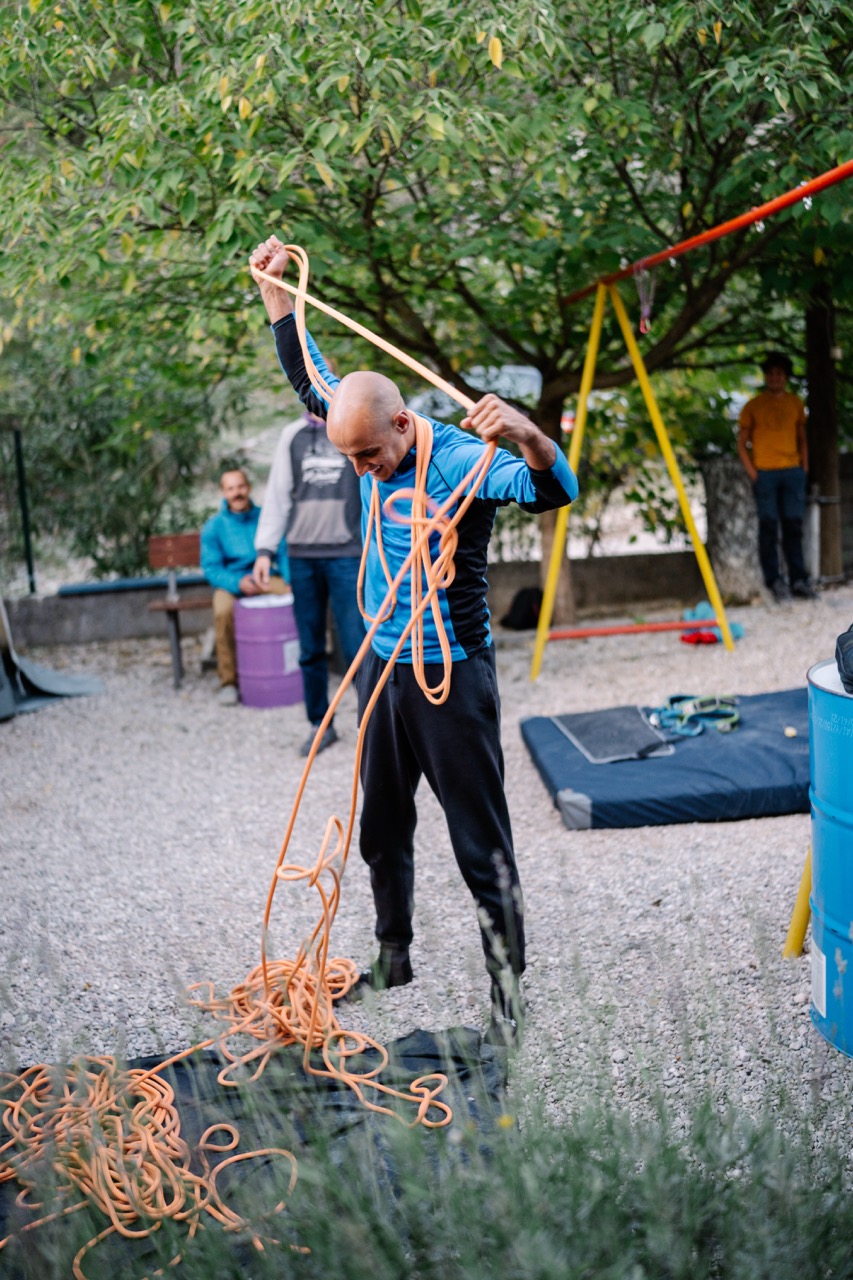 man wearing blue and black outfit untangling an orange climbing rope in an outdoor area