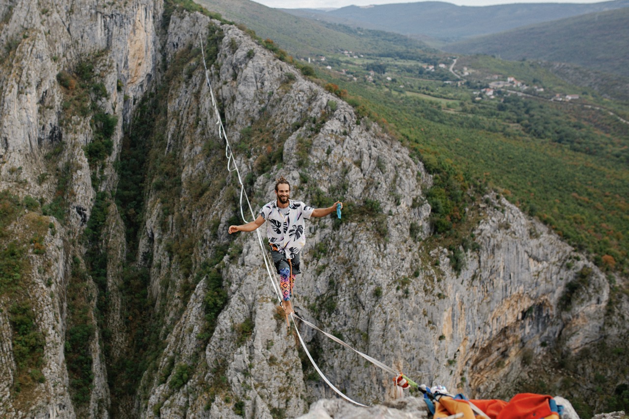 man walking barefoot on highline between rocky cliffs with valley and distant hills in background
