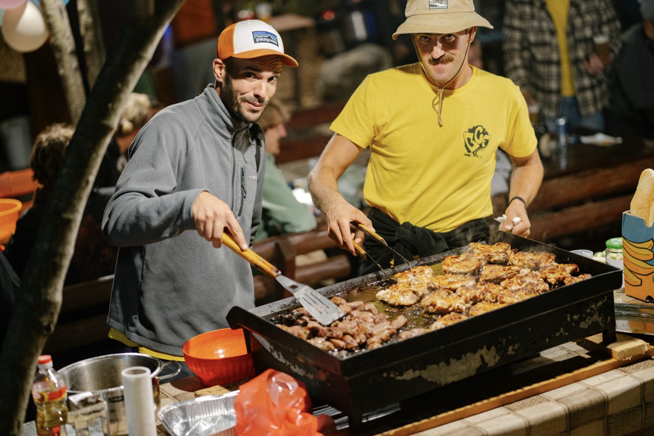 two men cooking assorted meats on large outdoor grill at night