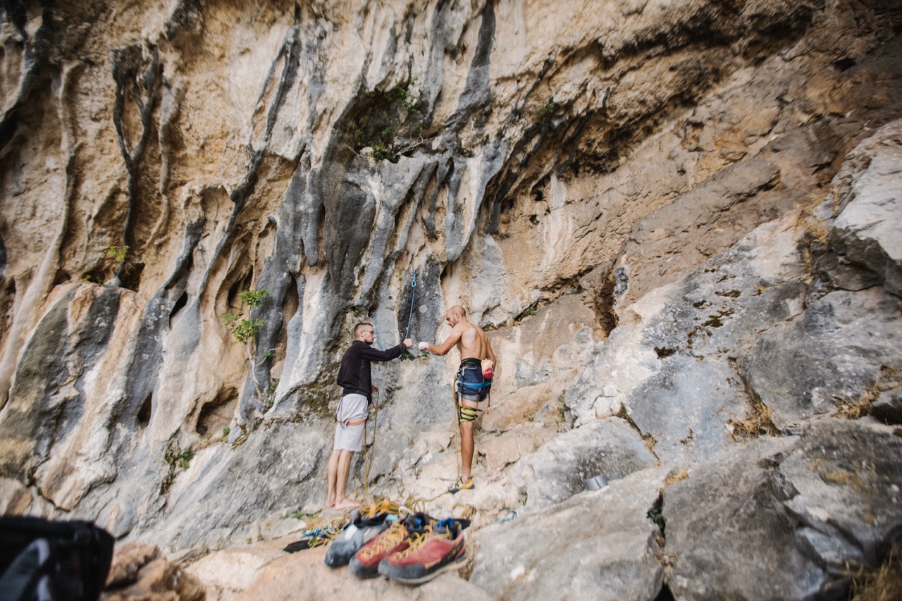 two men preparing climbing ropes and gear at the base of a rock climbing cliff
