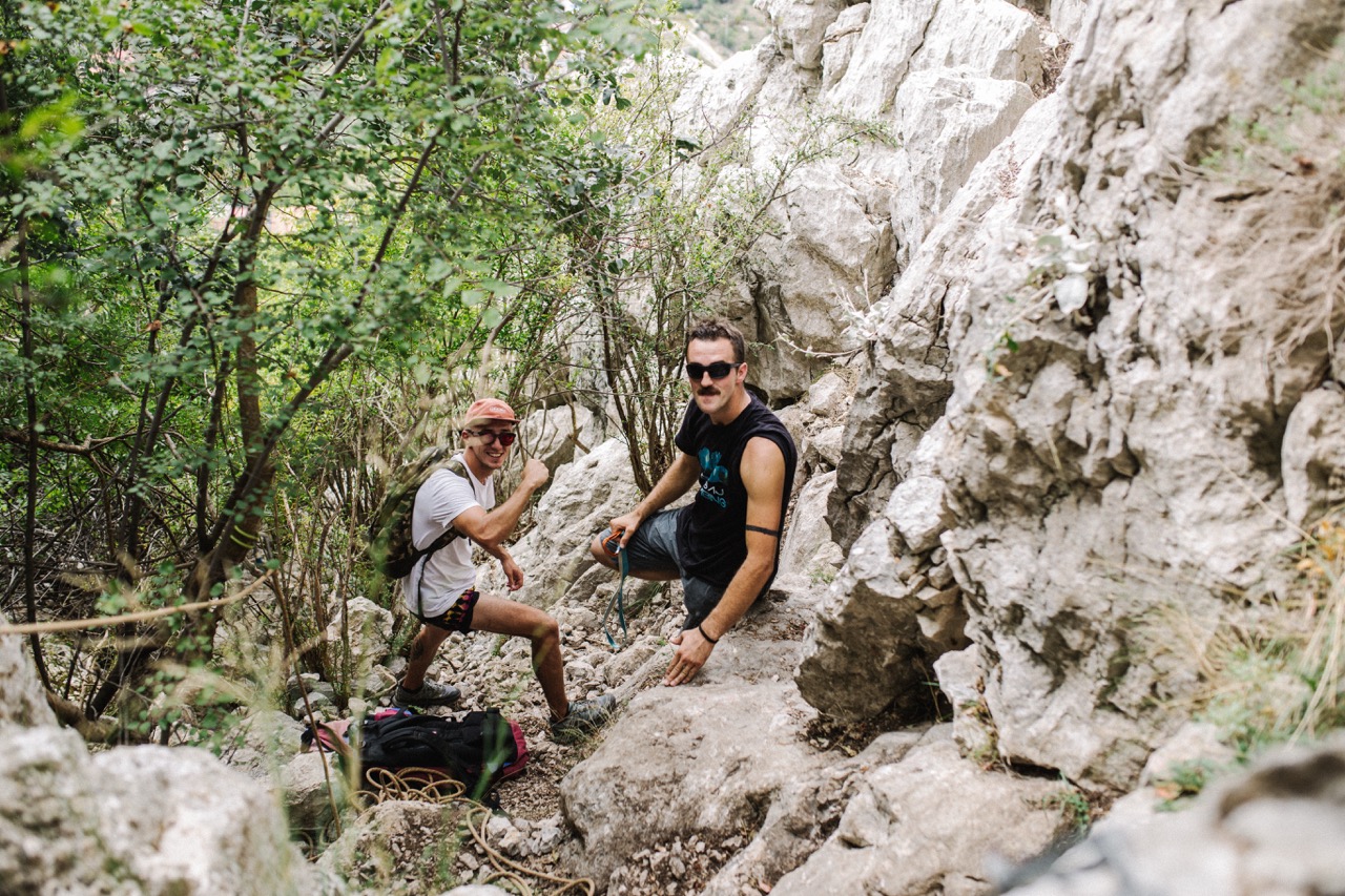 two men resting on rocky terrain surrounded by trees and vegetation during outdoor adventure