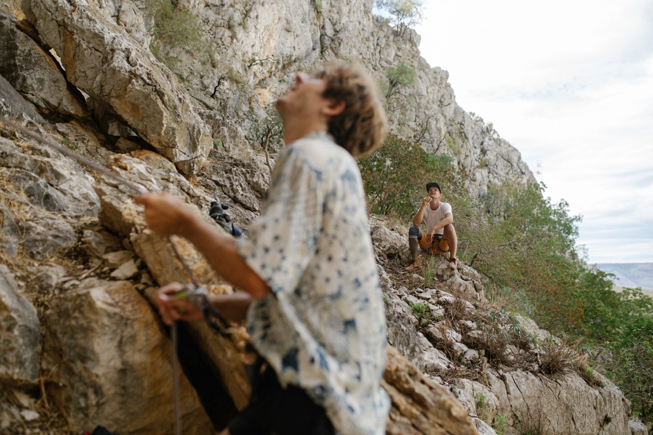 two men rock climbing in a mountainous area with one belaying and another resting on rocks