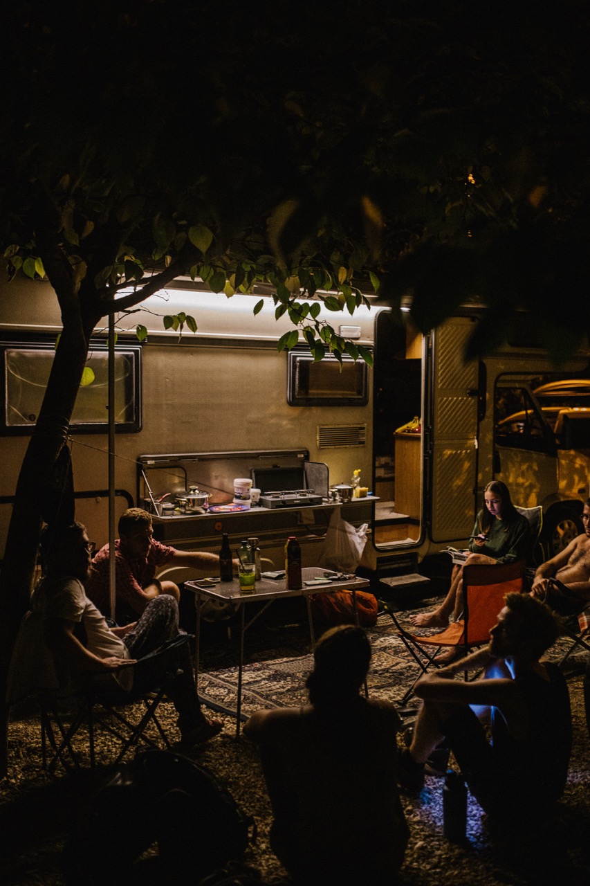group of people sitting around outside an RV at night under tree branches