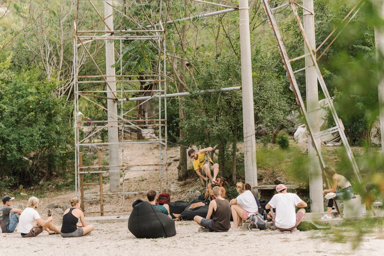 group of people seated outdoors watching an instructor demonstrate climbing safety techniques