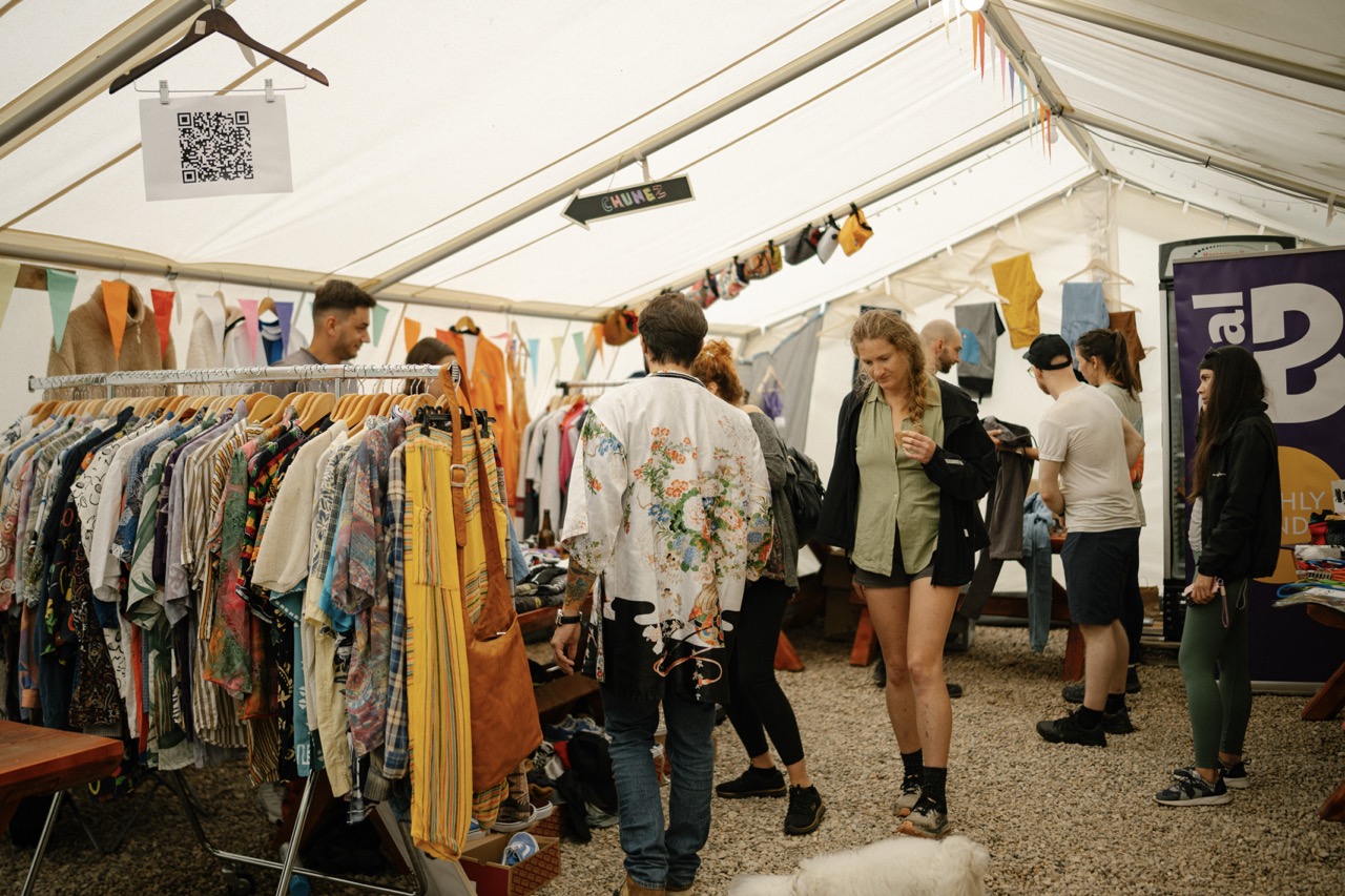 people shopping for clothes at an indoor market tent with racks of colorful casual wear