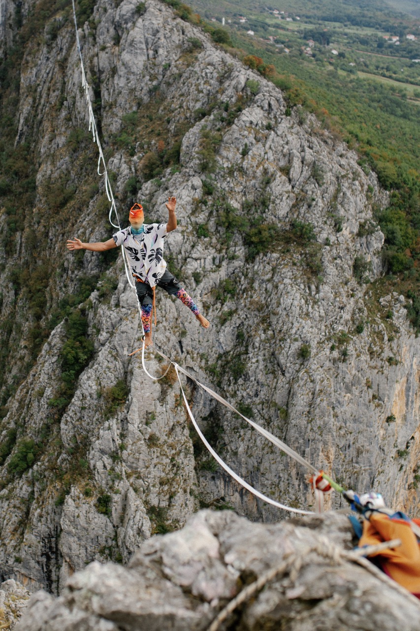 person balancing barefoot on a highline stretched between rocky cliffs
