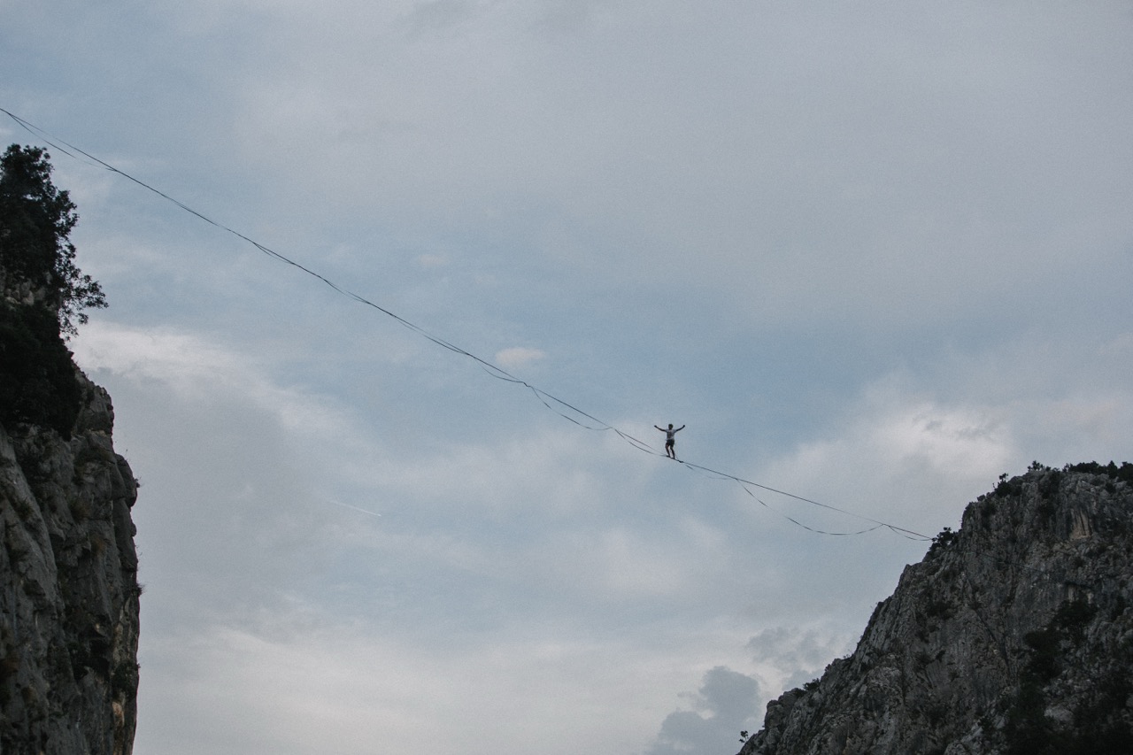 person walking on a highline stretched between two rocky cliffs against a cloudy sky
