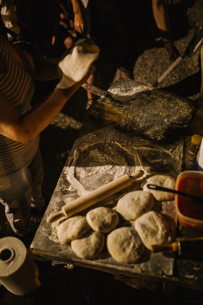person preparing dough balls on a floured surface with rolling pin and pizza peel nearby