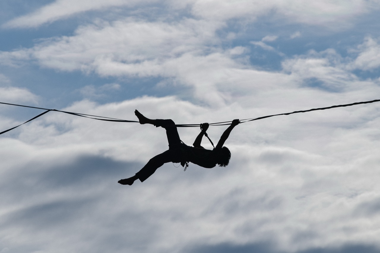 man climbing on a wire rope high in the sky with cloudy background