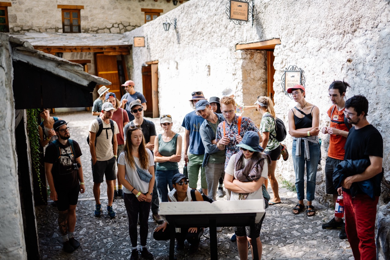 group of people gathered around an information board in a cobblestone courtyard with white stone walls