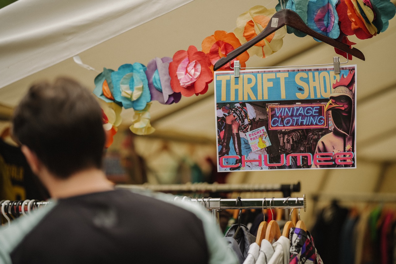 man browsing clothes rack at a thrift shop with vintage clothing sign and colorful paper flowers