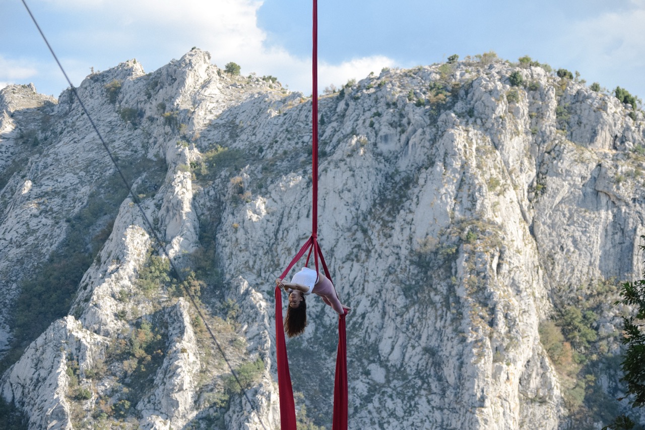 woman performing aerial silk acrobatics against a mountainous outdoor backdrop