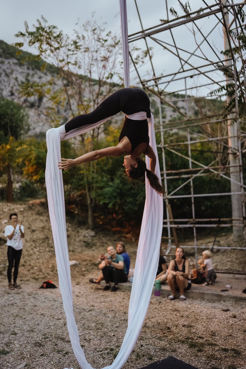 woman performing aerial silk acrobatics outdoors with audience watching