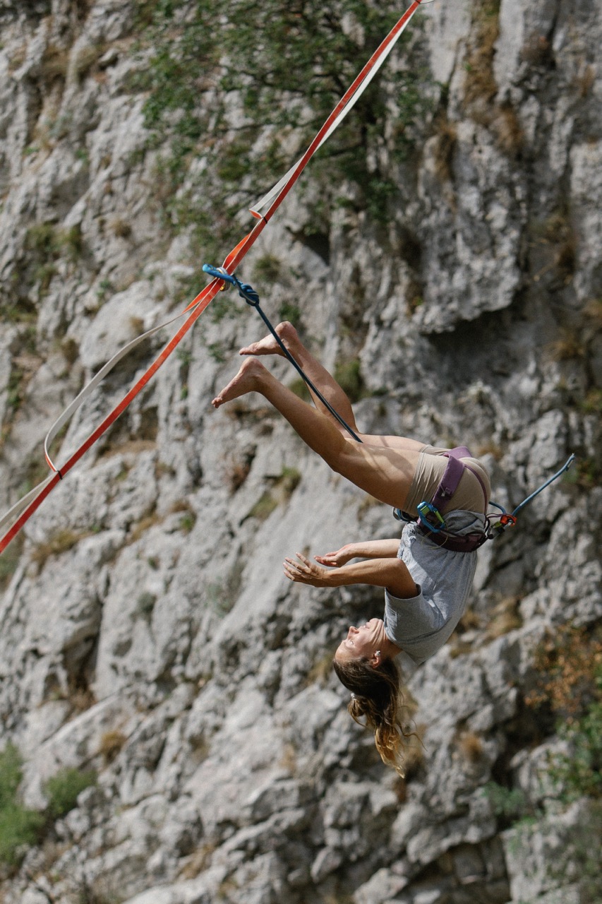 woman performing a backflip on a slackline in front of a rocky cliff
