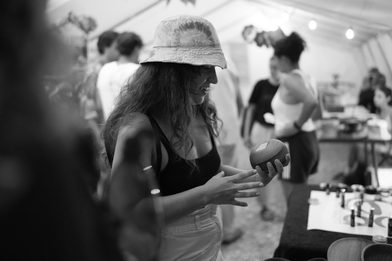 woman wearing a bucket hat examining a small wooden bowl at a market stall