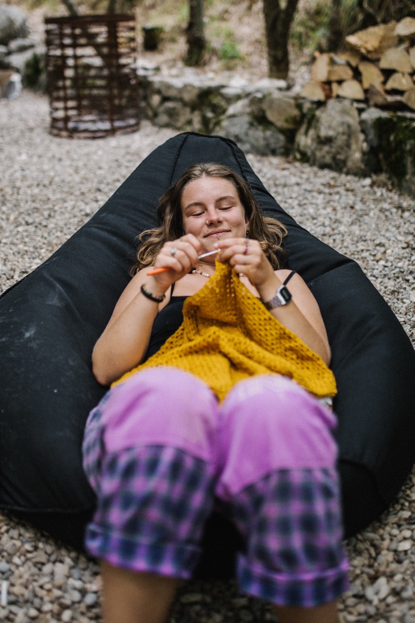 woman relaxing on black bean bag chair knitting a yellow fabric outdoors on gravel