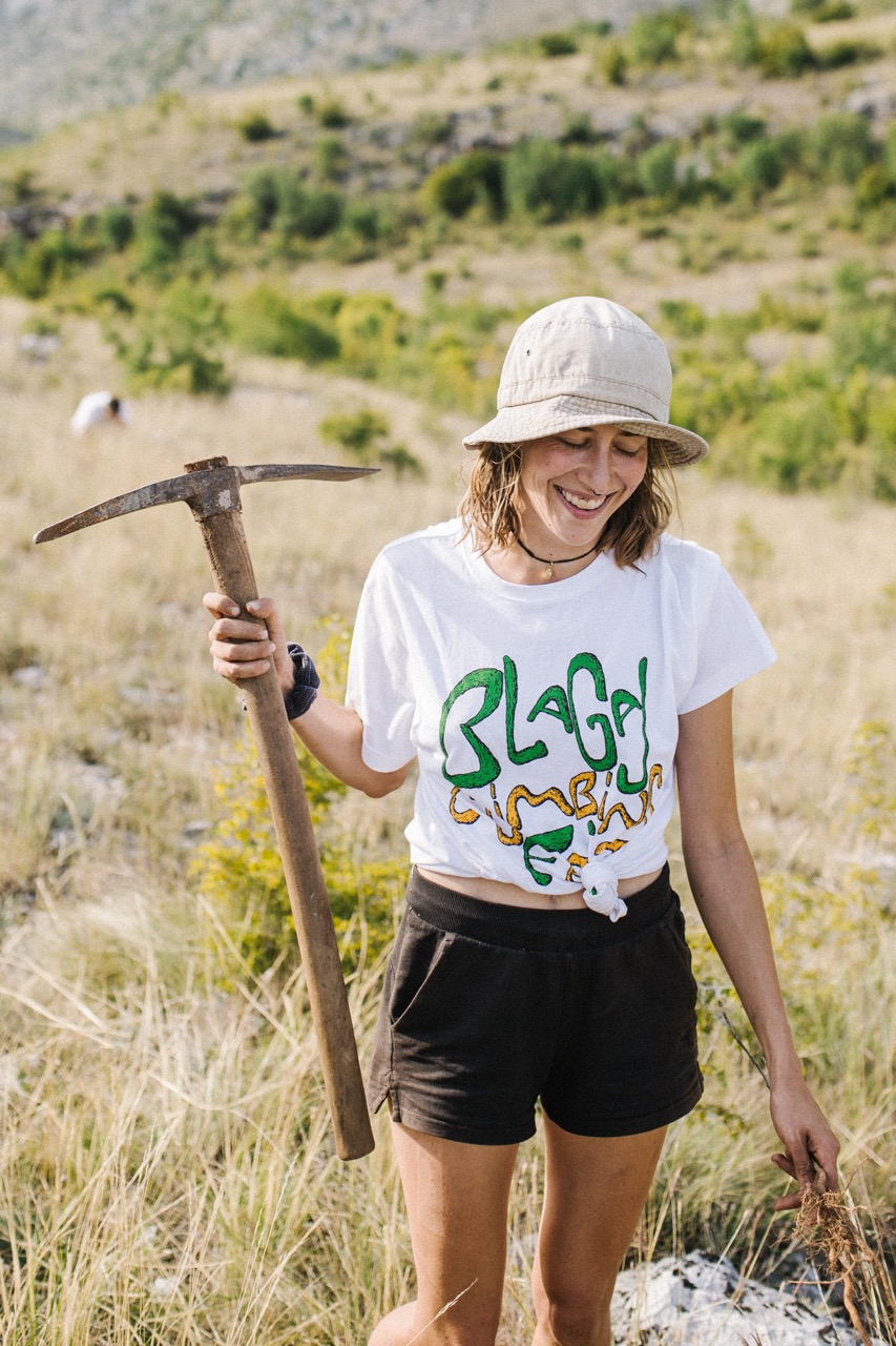 woman smiling outdoors holding a pickaxe in a grassy field