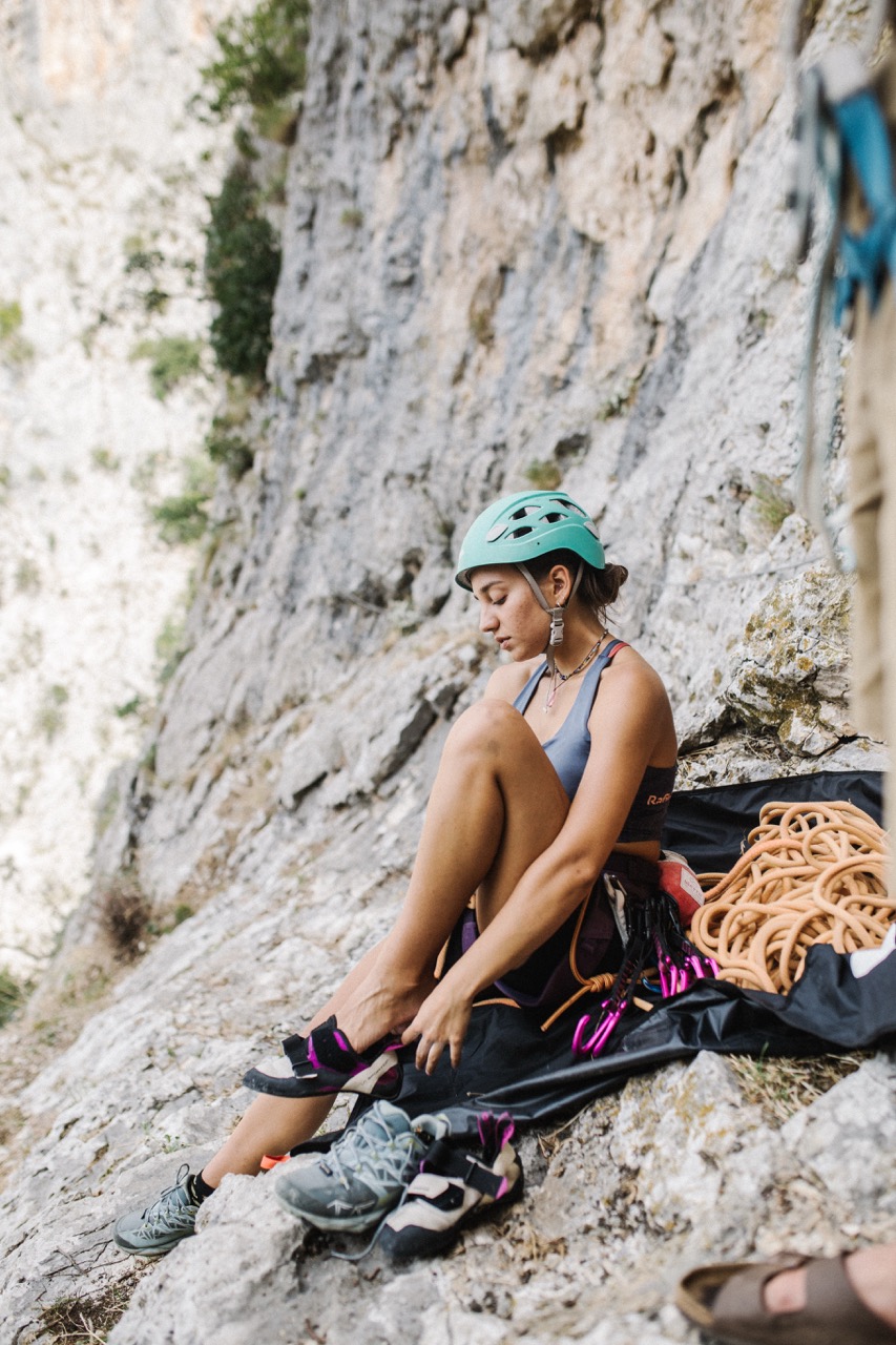 woman wearing helmet sitting on rocky ledge preparing for rock climbing with climbing gear beside her