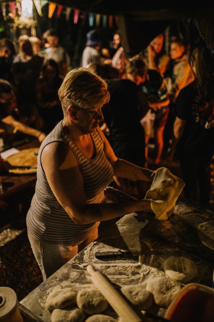 middle-aged woman preparing dough at night with people and festive lights in the background
