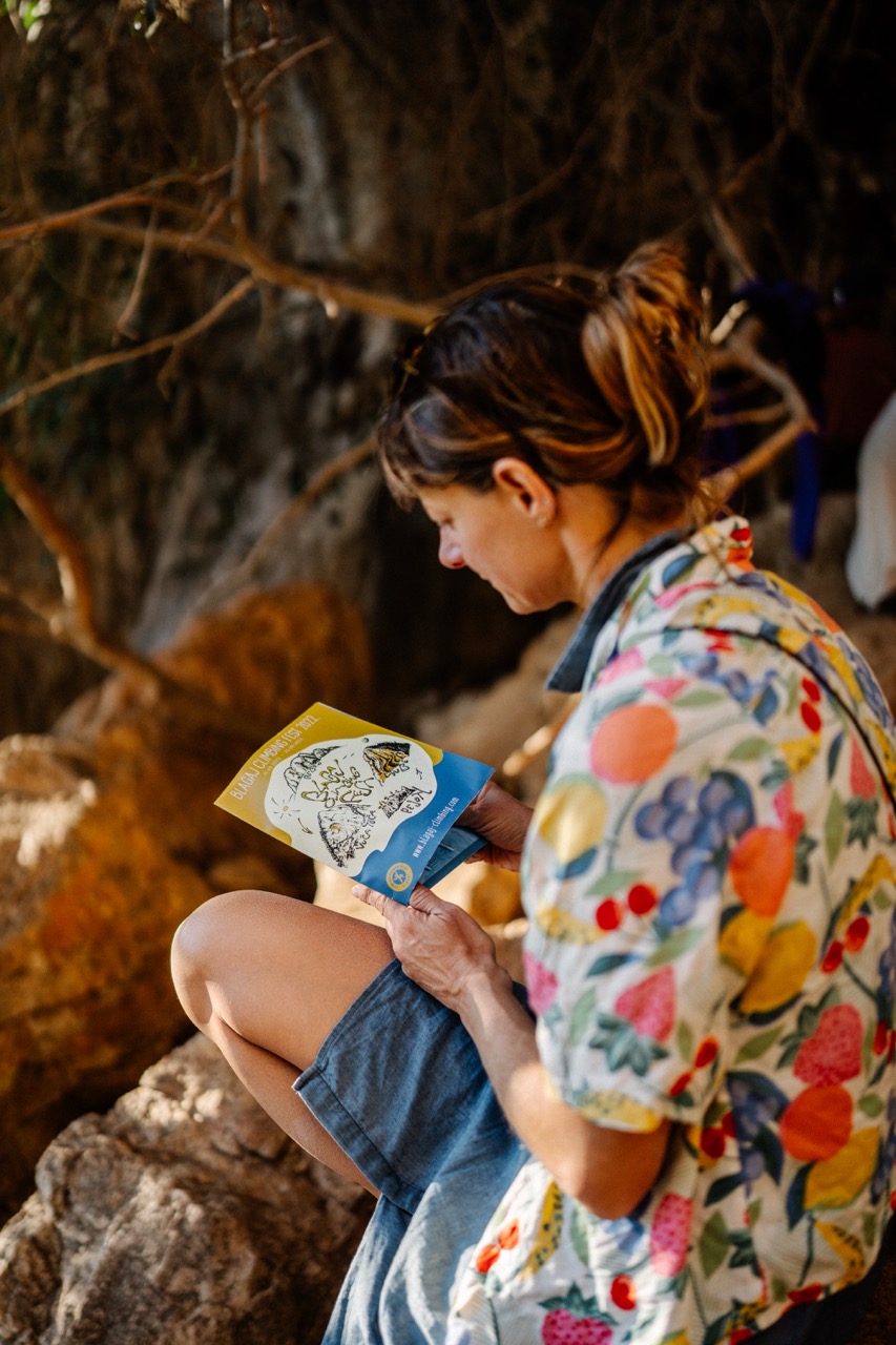 woman holding and reading a colorful brochure while sitting on rocky ground