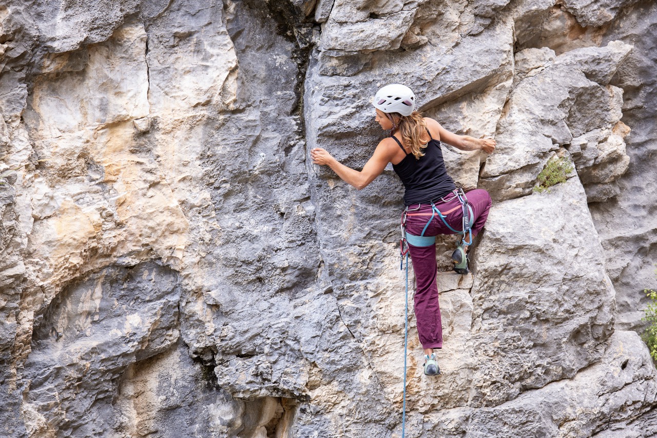 woman rock climbing on a steep gray and beige rocky surface wearing safety gear and helmet