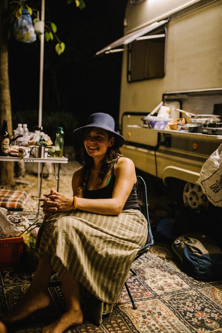 woman sitting on chair outdoors at night near camper and camping equipment